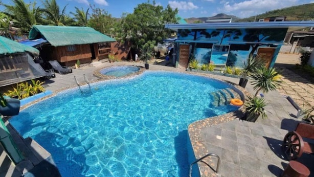 A swimming pool with a clear blue water surface, surrounded by lounge chairs and a small hot tub.