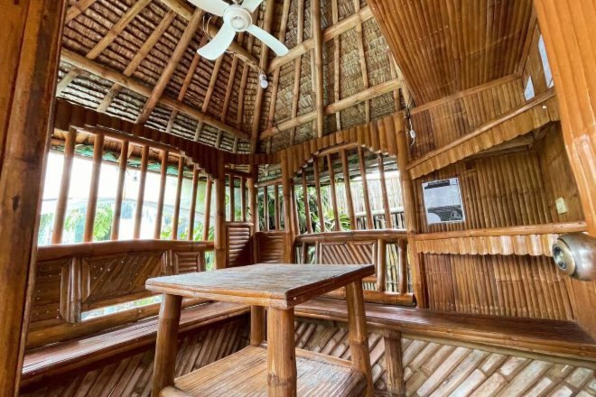 A wooden interior with a high ceiling, a ceiling fan, and a table with benches.