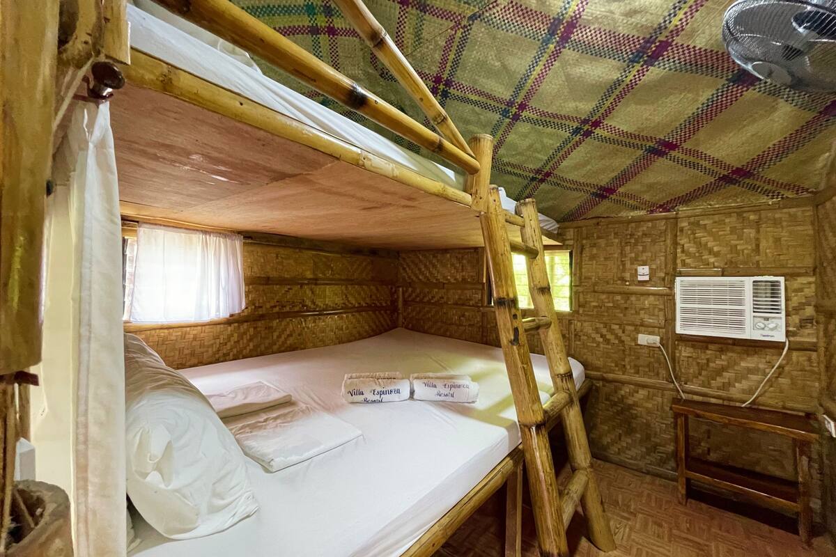 A bunk bed room with a wooden ceiling, a window with curtains, a wall-mounted air conditioner, and a small table.