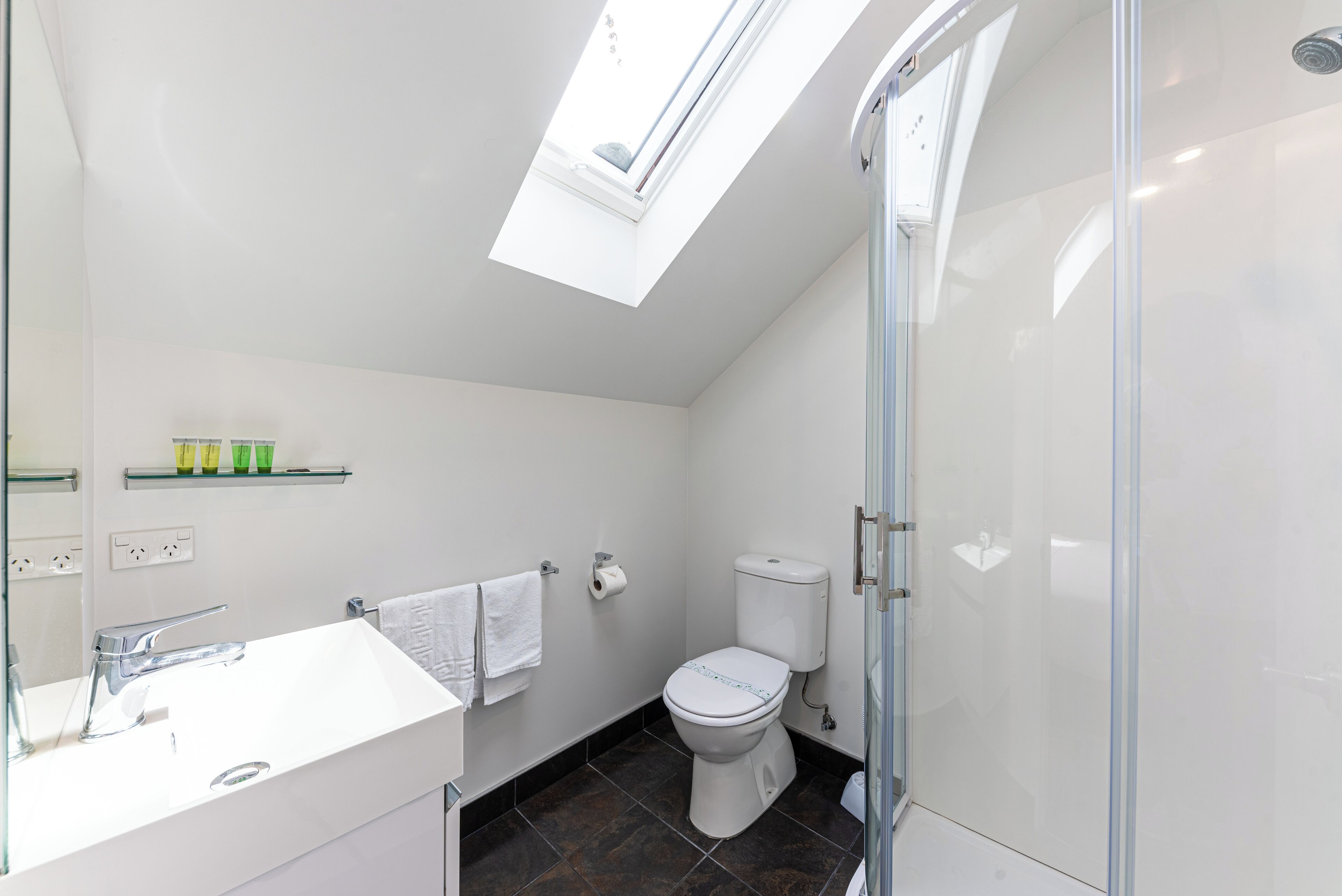 Ein modernes Badezimmer mit Oberlicht, einem weißen Waschbecken, einer Toilette und einer Duschkabine aus Glas.