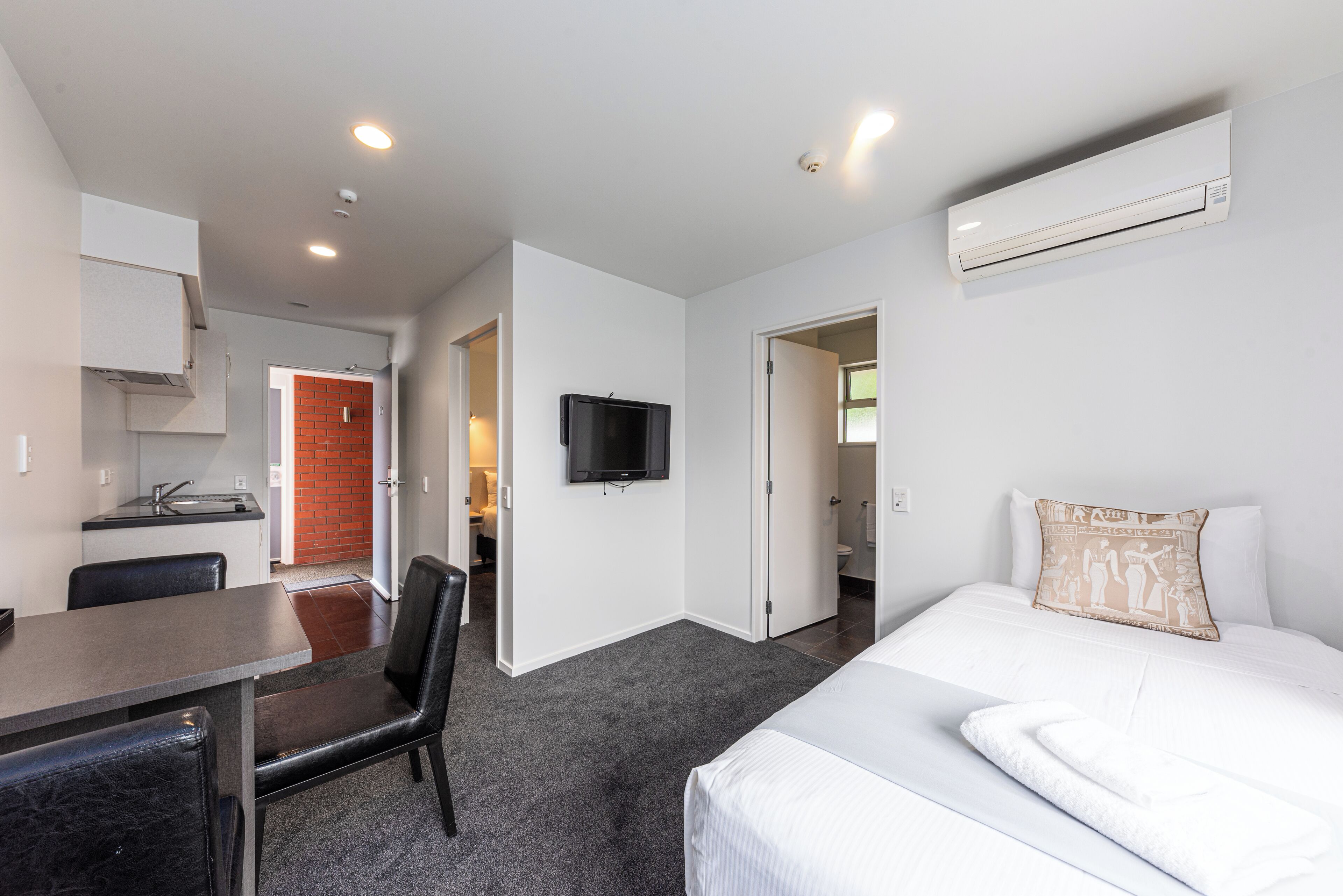 A hotel room with a bed, a TV, a kitchenette, and a bathroom.