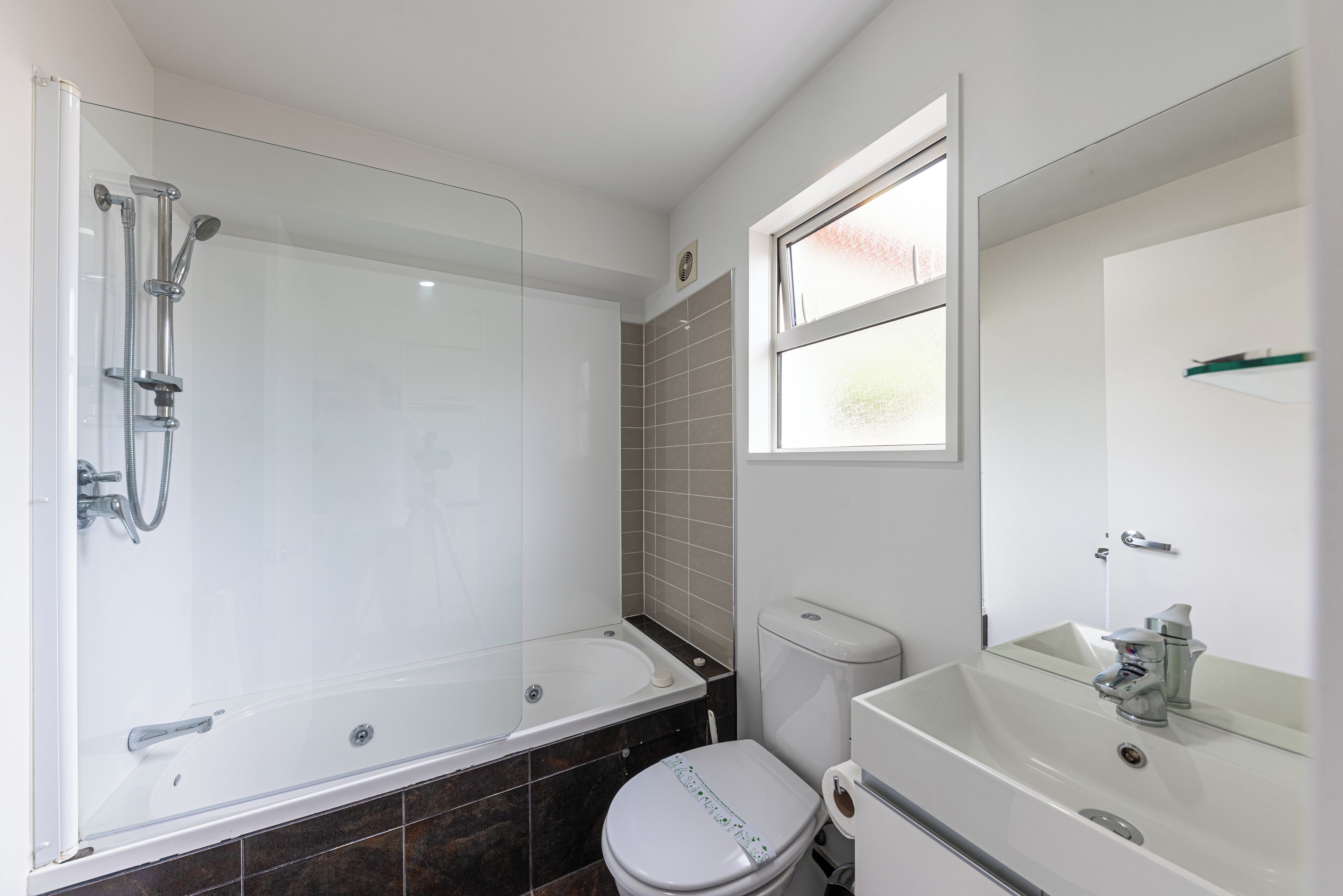 A modern bathroom with a glass-enclosed shower, a toilet, and a sink with a mirror.