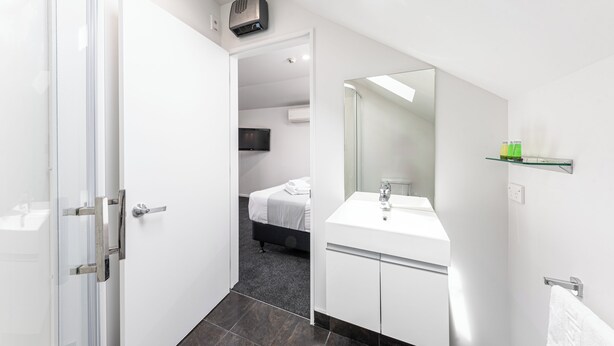 A modern hotel room with a glass shower enclosure, a white sink, and a large mirror. - 315 motel Riccarton (Christchurch)