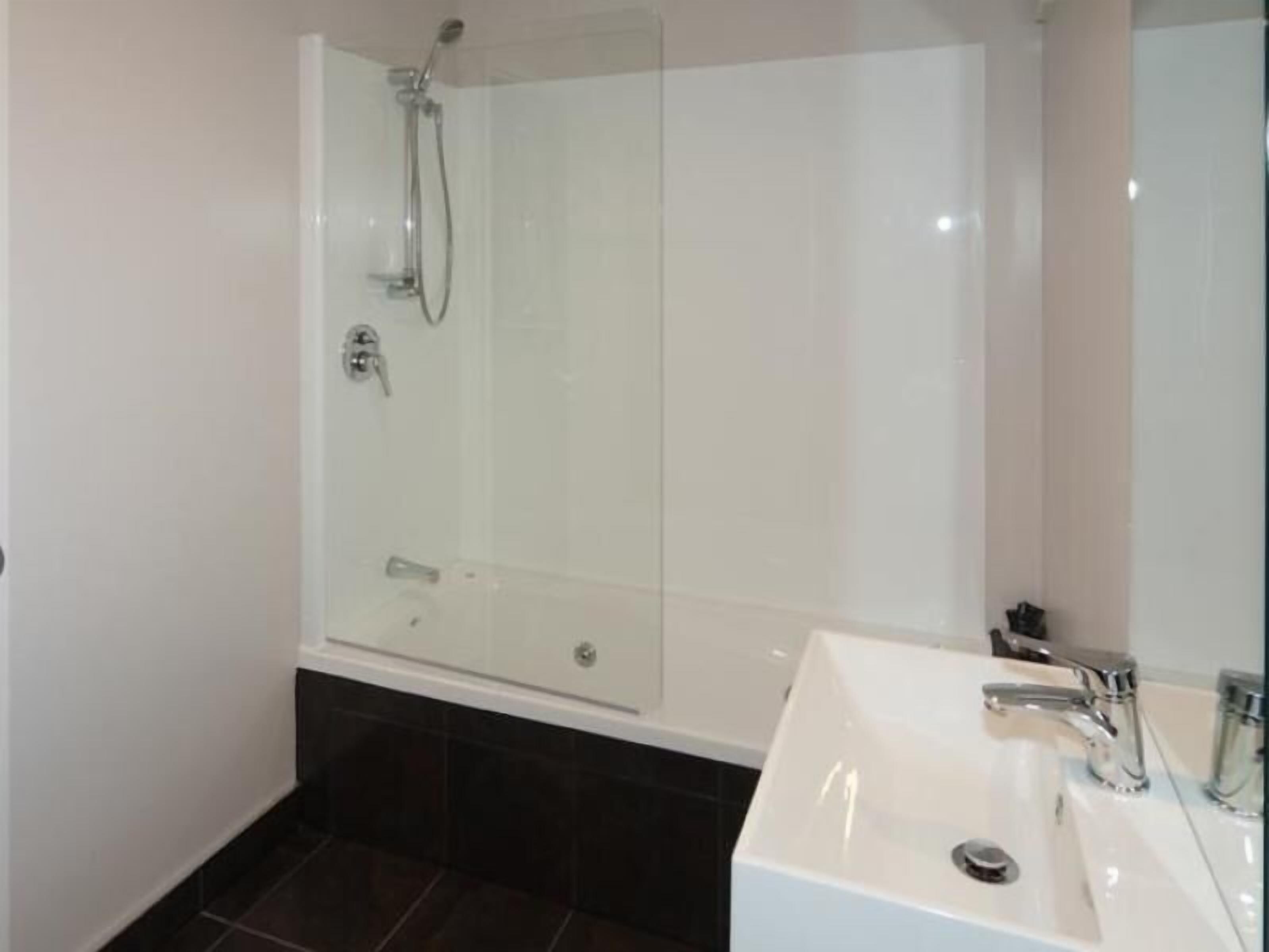 A modern bathroom with a glass-enclosed shower, a white sink, and dark tiled flooring.