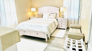 Un dormitorio con una cama, dos mesitas de noche con lámparas, una silla y un ventilador de techo.