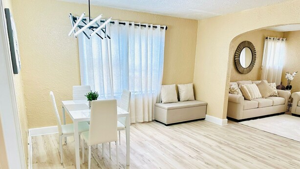 Una sala de estar moderna con comedor, paredes color beige y piso de madera clara.