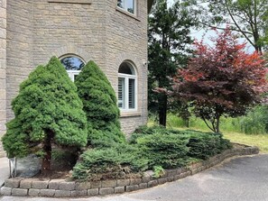 A stone building with a window and a door, surrounded by well-maintained shrubbery and a tree with red leaves.