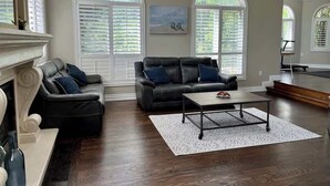 A spacious living room with a fireplace, two black leather sofas with blue cushions, a coffee table, and large windows with shutters. - 5 acre Luxury estate. 15 min from Niagara Falls (Welland)