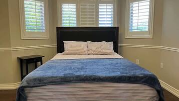 A bedroom with a bed, a nightstand, and three windows with blinds.