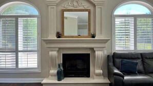 A room with a fireplace, two windows with shutters, and a leather sofa. - 5 acre Luxury estate. 15 min from Niagara Falls (Welland)