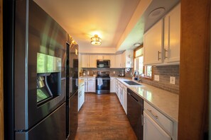 A modern kitchen with stainless steel appliances, white cabinetry, and a wooden floor.