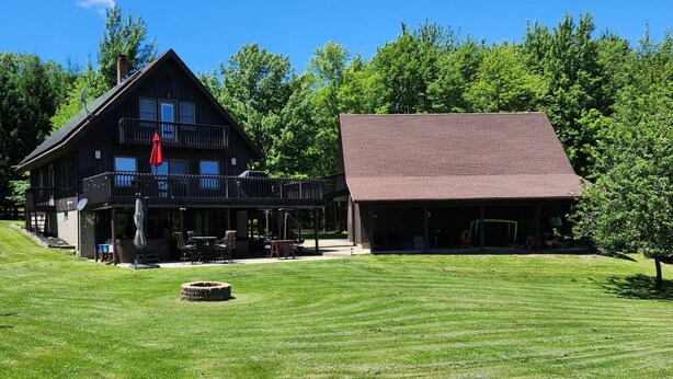 A two-story lodge with a large deck and outdoor seating area. - Dream Country Getaway 27 Acres in Conesus, NY! New Game Room! (Conesus)