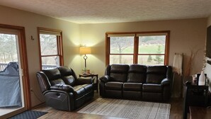 A living room with two leather sofas, a lamp, and a view of a green landscape through large windows. - Dream Country Getaway 27 Acres in Conesus, NY! New Game Room! (Conesus)