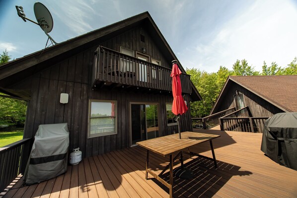 A wooden cabin with a balcony, a table, and a red umbrella.