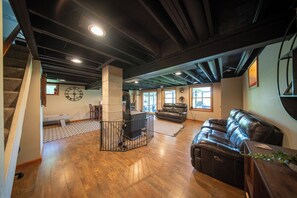 A spacious living area with a wooden floor, a black leather couch, a fireplace, and a large clock on the wall.