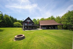 A two-story wooden house with a covered porch and a fire pit in the yard.