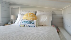 A neatly made bed with a pillow featuring the word "BEACH" and a decorative orange slice.