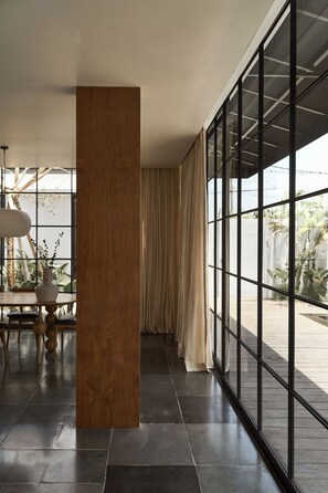 A modern interior with a large window, a wooden column, and a dining area with a table and chairs. - The Fernweh (Kerobokan)