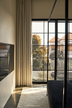 A modern bedroom with a large window, a flat-screen TV, and a dark-colored sofa. - The Fernweh (Kerobokan)
