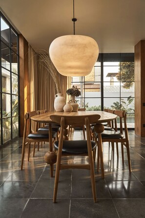 A dining area with a round table, wooden chairs, and a hanging light fixture. - The Fernweh (Kerobokan)