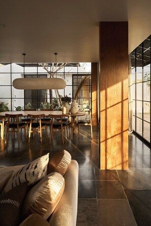 Un interior espacioso con una gran mesa de comedor, sillas de madera, un sofá con cojines y una escalera.