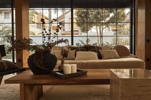 A cozy living room with a sofa, a wooden coffee table, and a large window with a view of buildings and trees. - The Fernweh (Kerobokan)