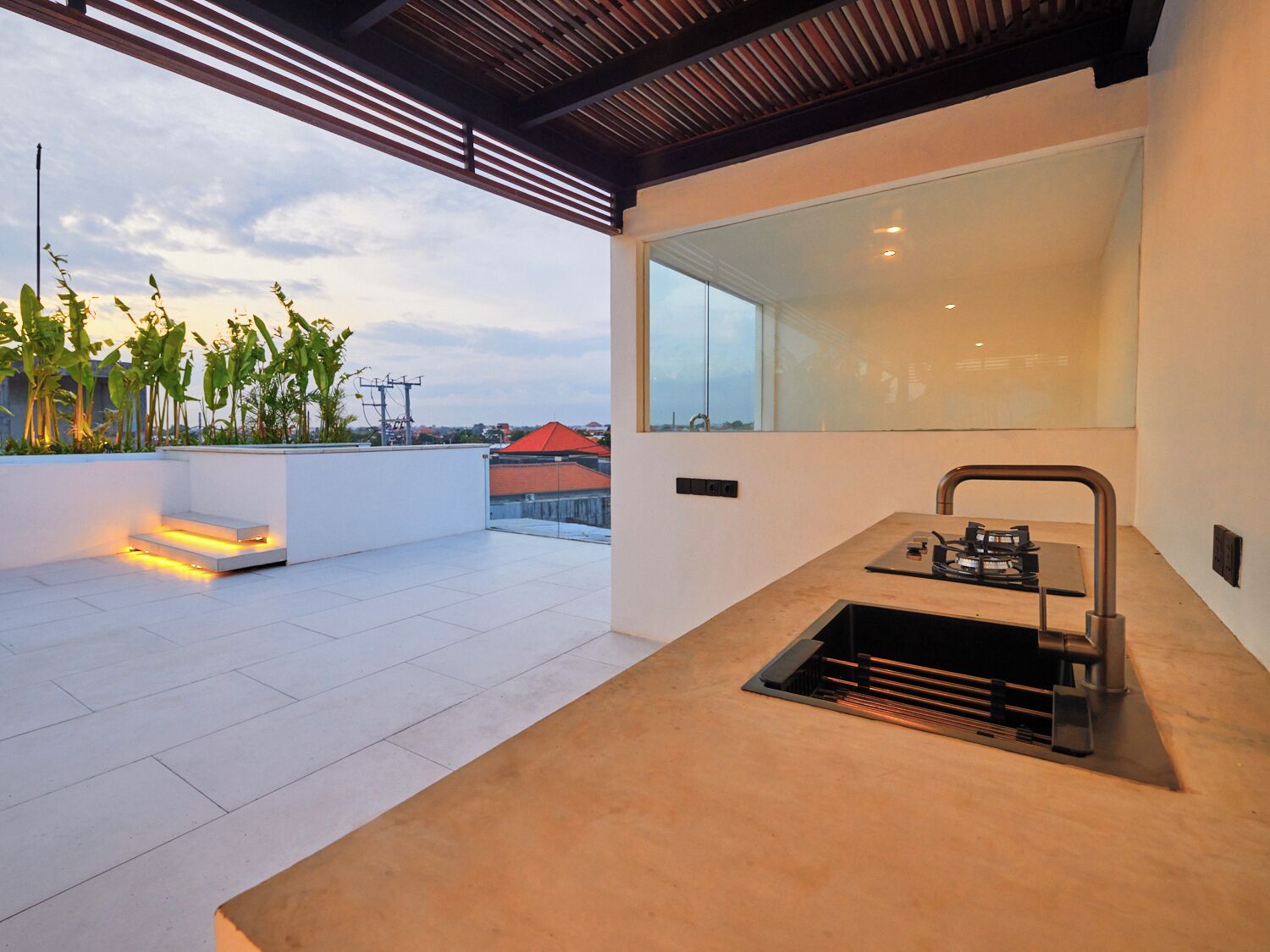 A modern outdoor kitchen with a built-in sink and a large window overlooking a cityscape.