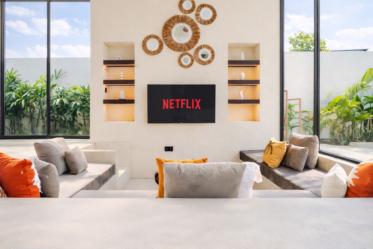 Een moderne woonkamer met een flatscreen televisie aan de muur, een zithoek en uitzicht op groen.