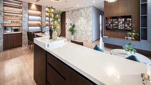 Eine moderne Küche mit Marmorarbeitsplatte, Holzschränken und einer zentralen Kochinsel. Es sind Pendelleuchten, ein Kronleuchter und eine Wandvitrine zu sehen.