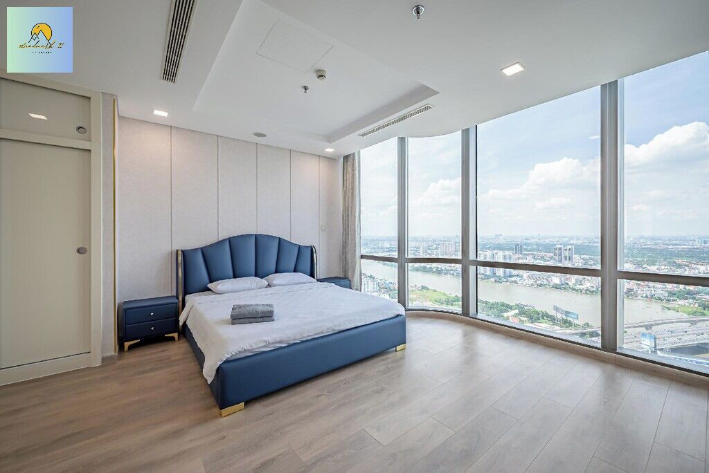 Ein modernes Schlafzimmer mit einem großen Bett, einem Nachttisch und Blick auf eine Stadtlandschaft durch große Fenster.
