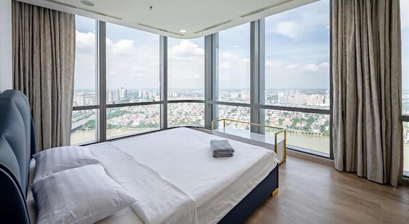 A bedroom with a large bed, a chair, and a view of a cityscape through large windows. - Landmark 81 Skyscraper (Ho Chi Minh City)