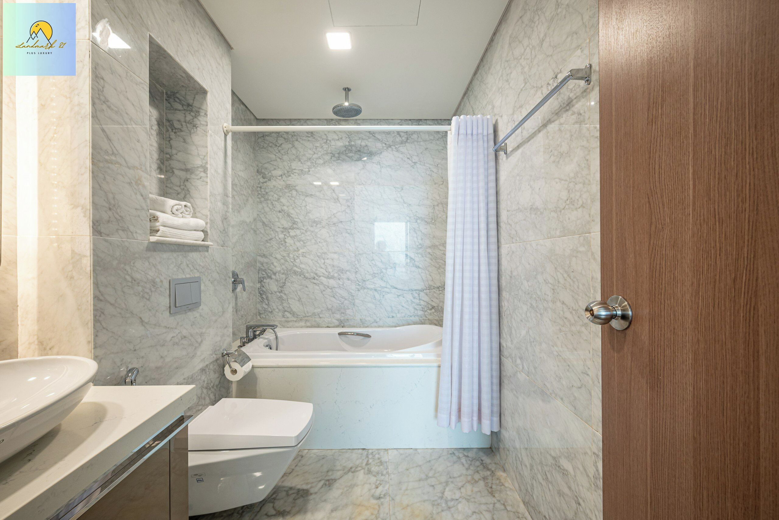 A modern bathroom with a marble wall, a bathtub, a toilet, and a sink.