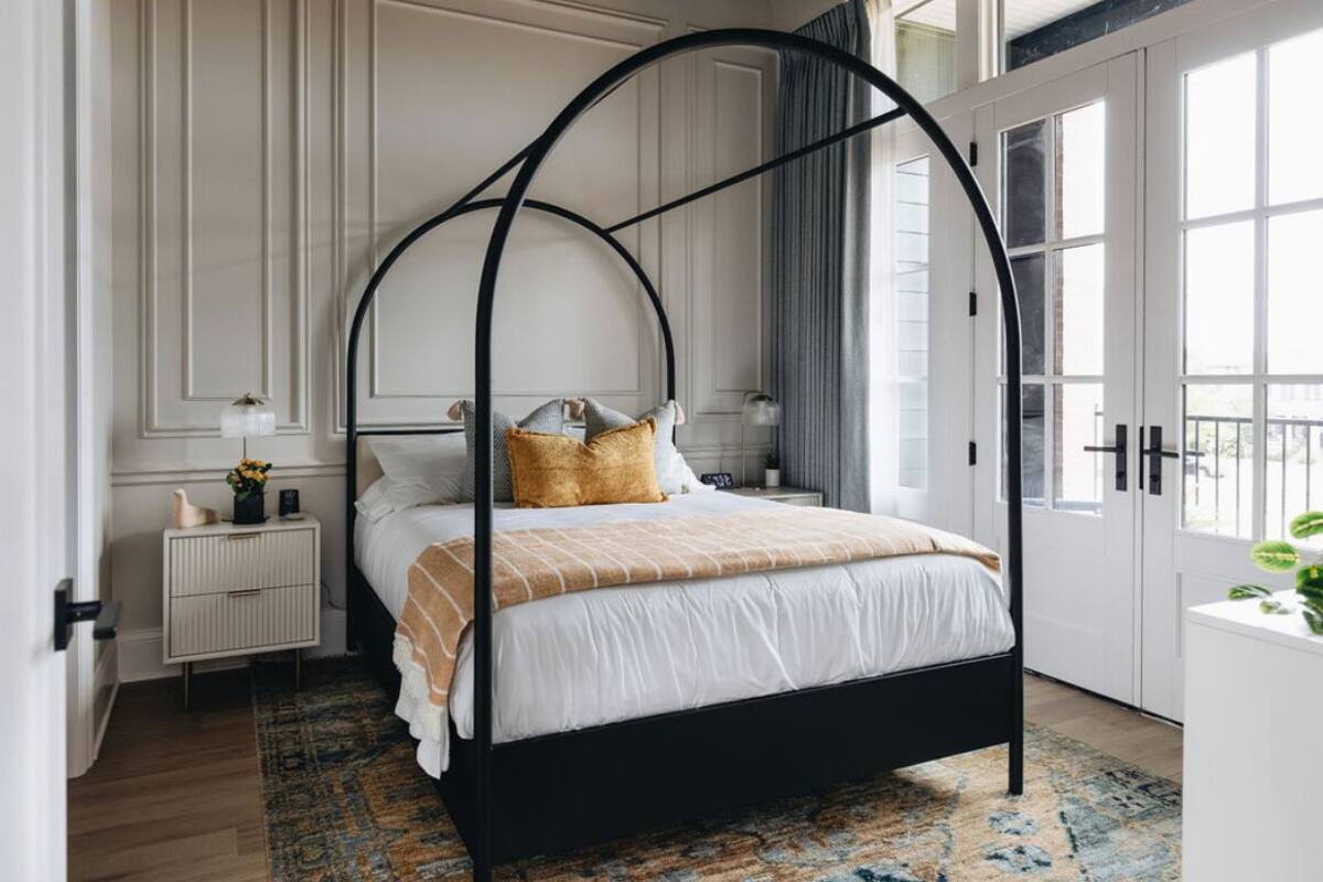Un dormitorio con cama con dosel, una mesita de noche y una ventana con cortinas.