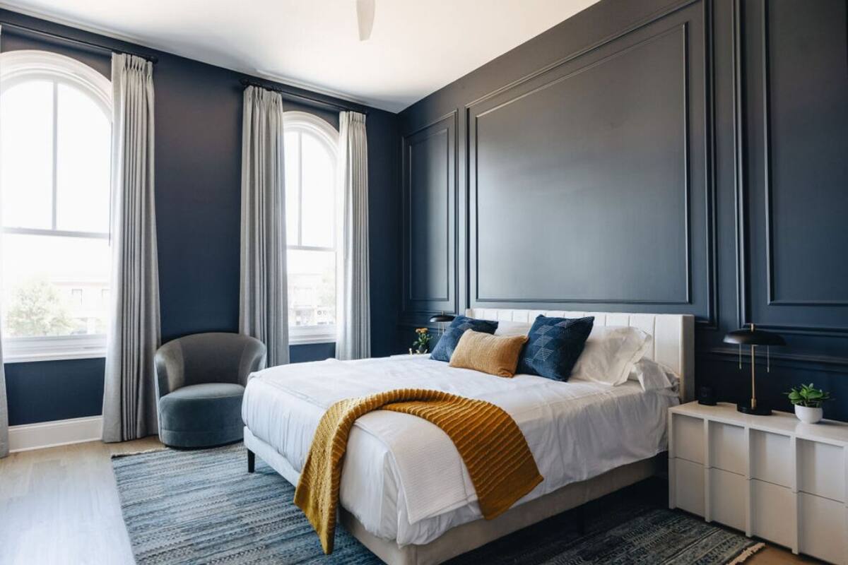 Un dormitorio moderno con una cama grande, una silla y una mesita de noche con una lámpara y una planta.
