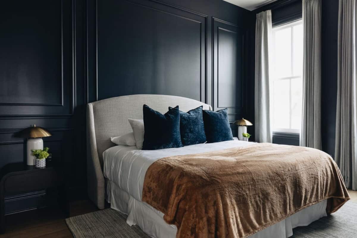 Un dormitorio moderno con una cama grande, paredes oscuras y una ventana con cortinas.