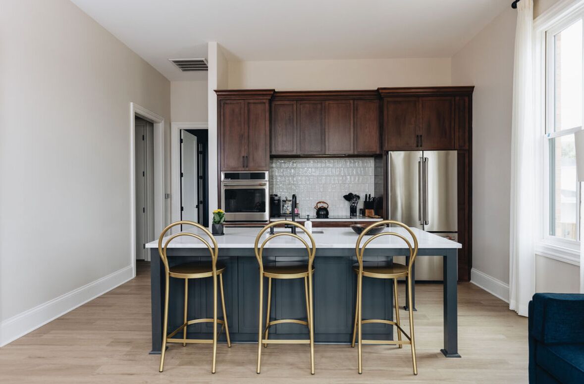 A modern kitchen with dark wooden cabinets, a central island with bar stools, stainless steel appliances, and a view to the left.