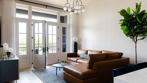En moderne stue med en lædersofa i brunt, et rundt sofabord og et stort vindue med udsigt.
