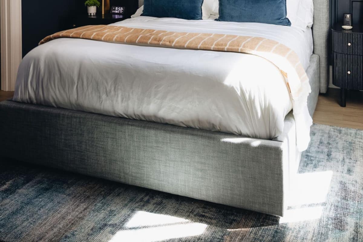 Un dormitorio moderno con una cama grande, paredes oscuras y un cabecero de color claro.
