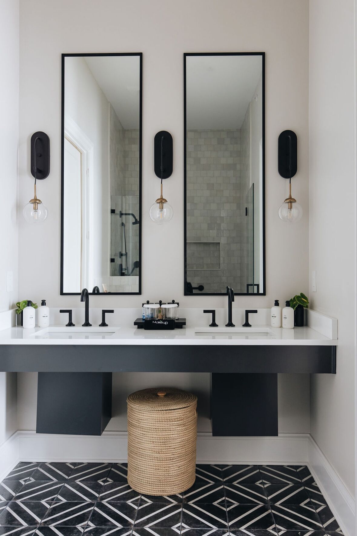 A modern bathroom with a large vanity, two mirrors, black faucets, and a black and white tiled floor.