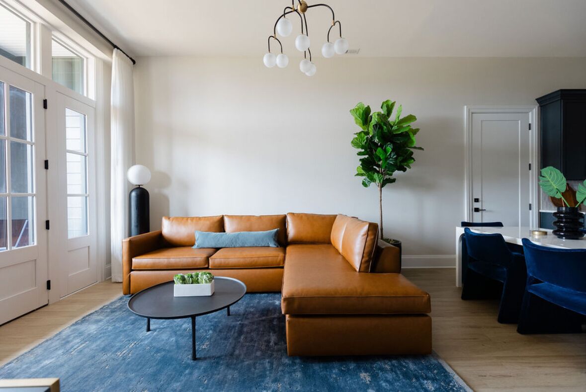 A modern living room with a leather sectional sofa, a round coffee table, and a large plant.