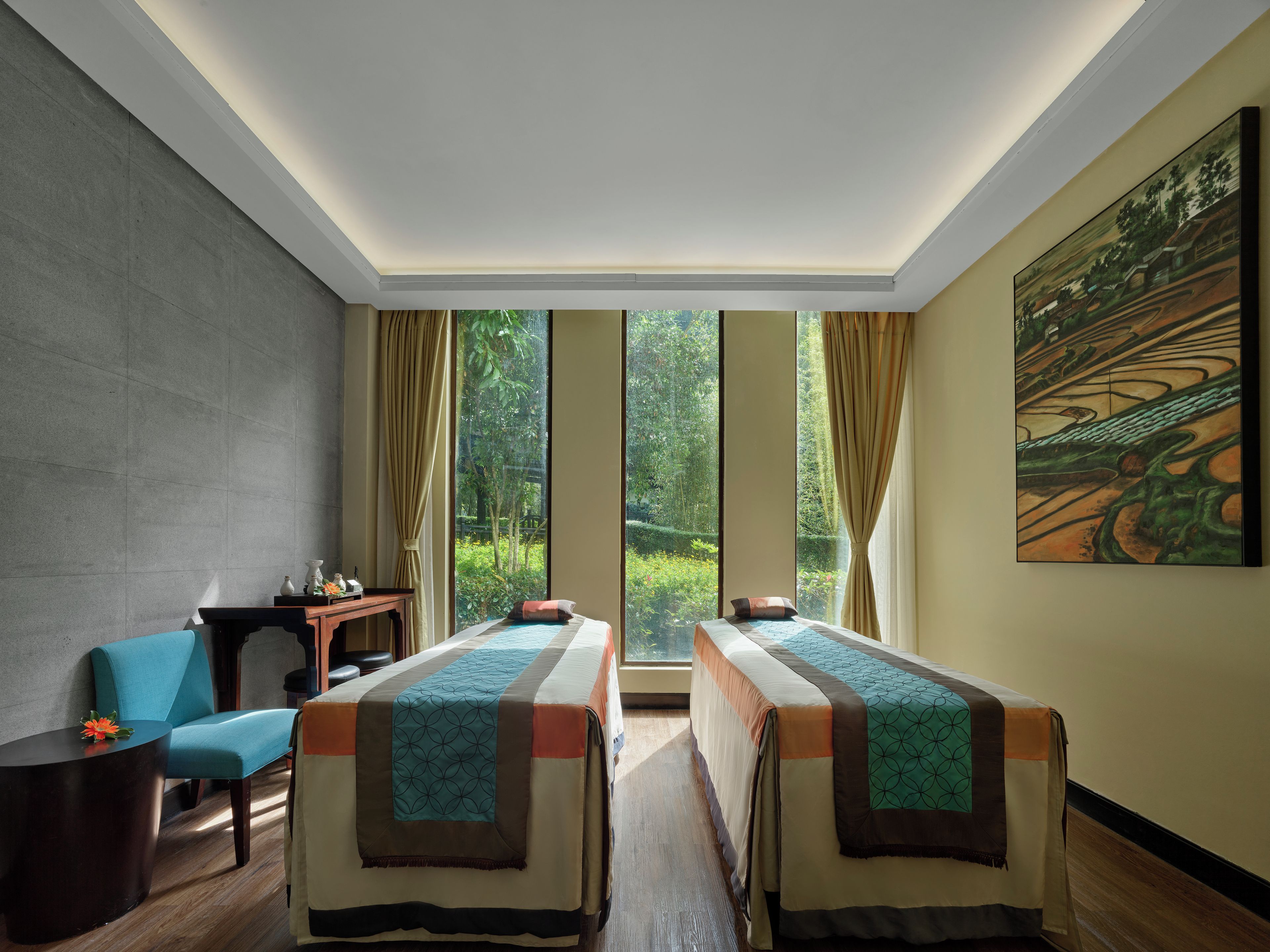 A hotel room with two beds, a desk, a chair, and a large window with a view of greenery.