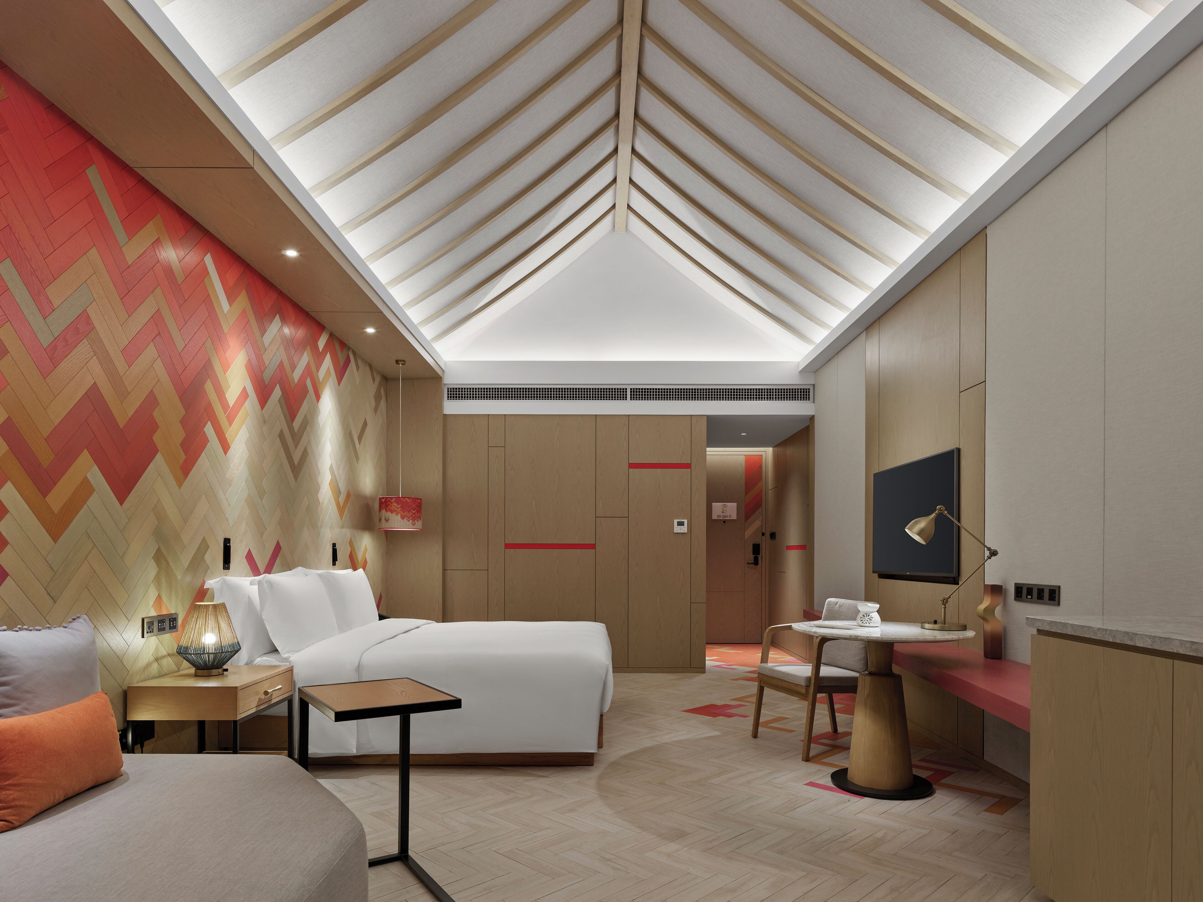 Een moderne hotelkamer met een groot bed, een bureau, een stoel en een televisie. De wand is voorzien van een patroon en het plafond heeft een uniek ontwerp.