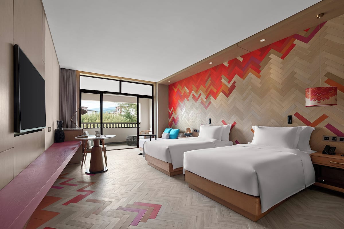 Habitación de hotel moderna con dos camas, un televisor grande, un escritorio y vistas al exterior.