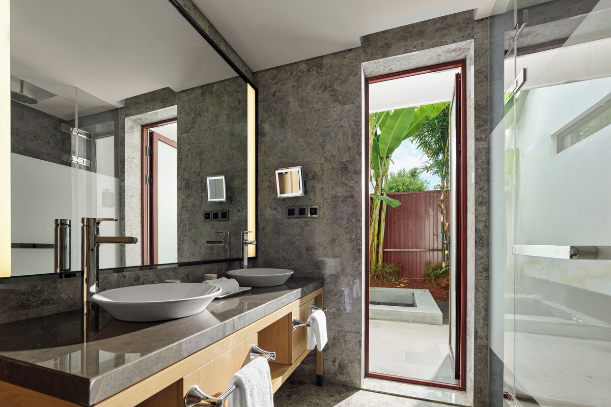 Un baño moderno con dos lavamanos, un espejo grande y una cabina de ducha con mampara de vidrio.