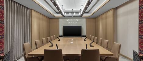 A conference room with a long table, multiple chairs, a projector screen, and a modern ceiling light fixture.