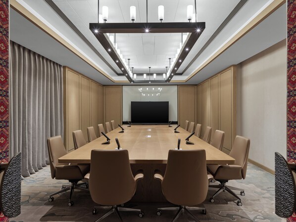 Un salón de conferencias con una larga mesa, varias sillas, una pantalla de proyector y una lámpara de techo moderna.
