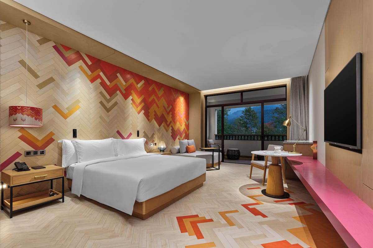 Una habitación de hotel moderna con una cama grande, mesita de noche, lámpara y televisor.