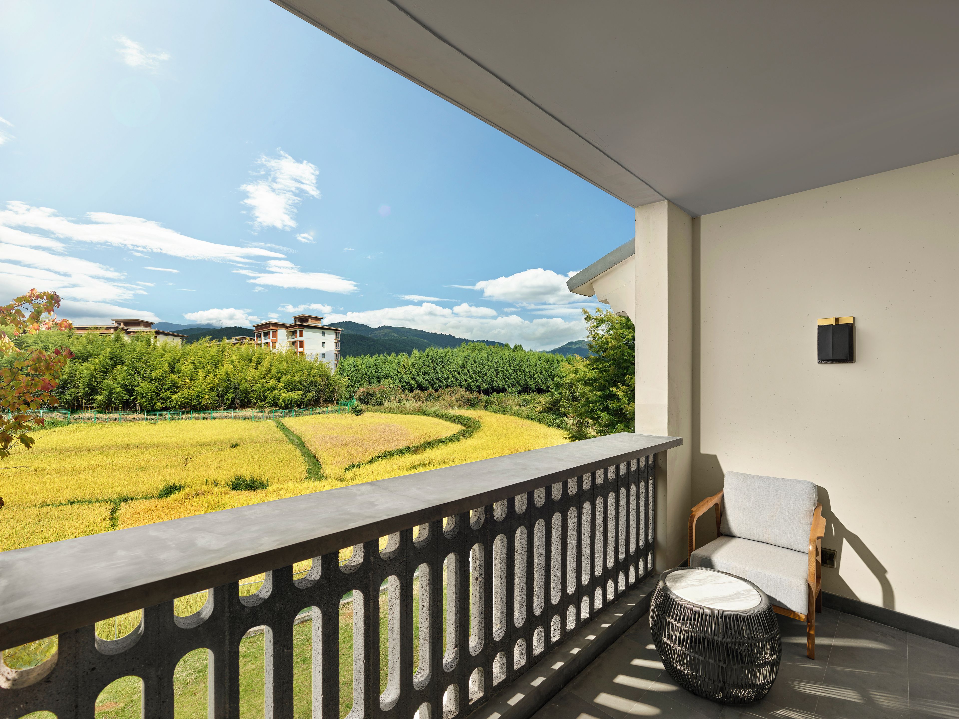 A balcony with a view of a rice field, a chair, and a round table.