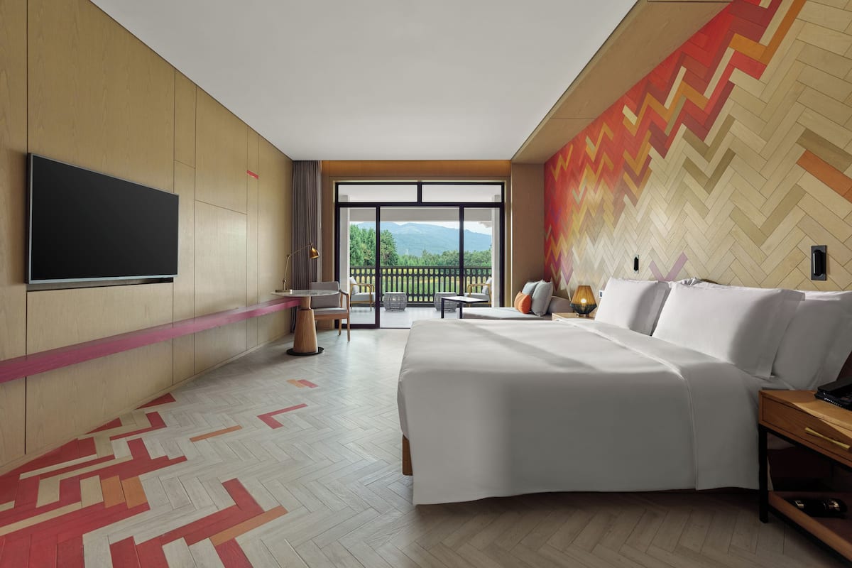 Una habitación de hotel moderna con una cama grande, un televisor de pantalla plana, un balcón con vistas a las montañas y una pared con motivo de espiga.