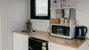 Una cucina compatta con forno a microonde, macchina da caffè e barattoli sul piano di lavoro.